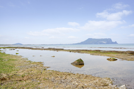 Landscape of Gwangchigi beach with Seongsan Ilchulbong, view from Olle trail No. 1. Gwangchigi is a unusual rocks beach and Ilchulbong is a volcanic cone located on the eastern end of Jeju Island.の写真素材