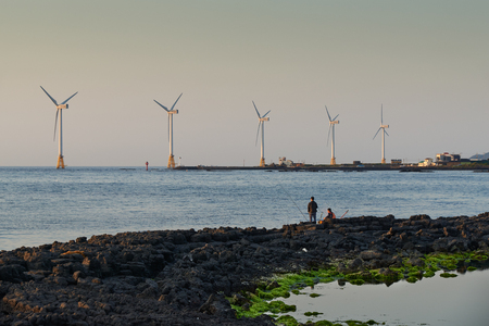 Jeju, Korea - May 25, 2017: Seascape of Sinchang Windmill Coast with fisherman, a famous place for driving course because of its beautiful natural scenery with wind generator.のeditorial素材