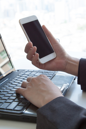 Close-up Businessman hand using smartphone screen and notebook computer and other supplies with Business report meeting and briefing at office, man's hands working with touchpad, flare lightの写真素材