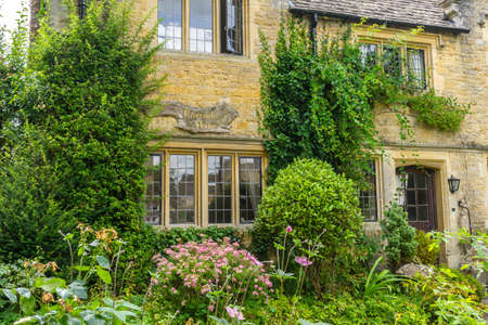 GLOUCESTERSHIRE,ENGLAND-AUGUST 5,2016 : Old house and green garden with tiny flowers during summer time in Bourton on the Water.のeditorial素材