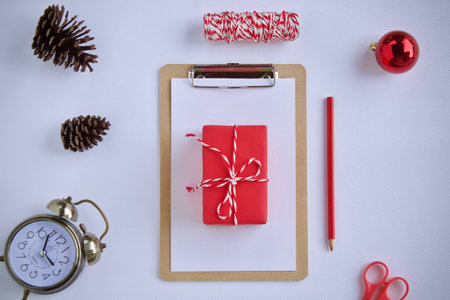 Red gift box with red ribbon on clipboard and christmas decoration on white backgroundの写真素材
