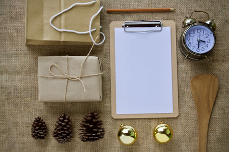 Christmas or New Year mockup with gift boxes, pine cone, alarm clock and notebook on sackcloth backgroundの写真素材