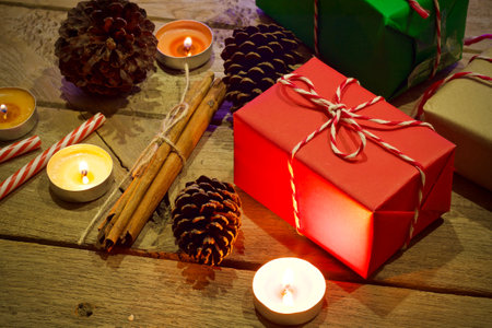 christmas still life with candles, gift boxes and pine cones on wooden background