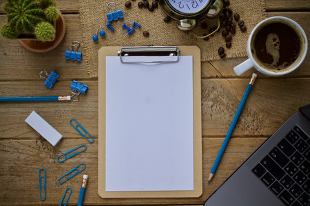 Blank clipboard with coffee cup and stationery on wooden table.