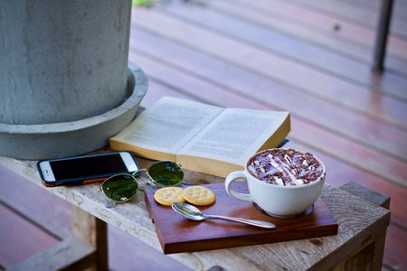 Cup of hot chocolate with book and mobile phone on wooden tableの写真素材