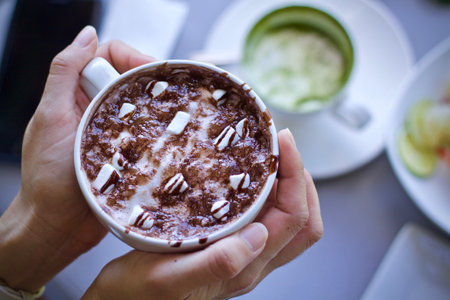 Hot chocolate with marshmallows in a cup in the hands.