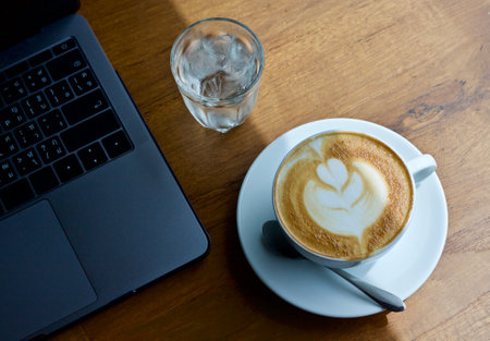 Coffee cup and laptop on wooden table in coffee shop.
