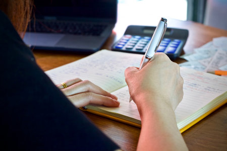 Woman's hands writing in a notebook with a calculator on the table