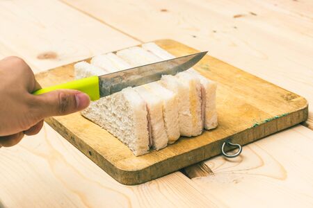 hand cutting sandwiches by knife on wooden chopping board