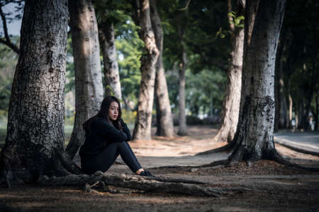 Asian woman sitting under a tree in the park, lifestyle concept.