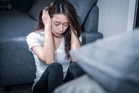 depressed young asian woman sitting on sofa in living room.