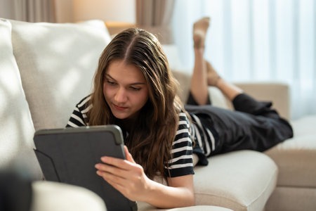 Serene woman reads an e-book on her tablet while relaxing on a peaceful sofa.