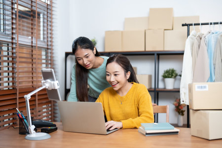 Two young adults running an online clothing business, using technology for marketing and logistics in a home setting.の写真素材