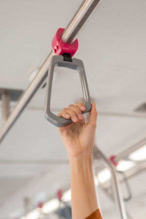 Close-up of hand gripping handrail in public transportation. High angle view with blurred background. Safety and hygiene in public spaces concept. Place for text.