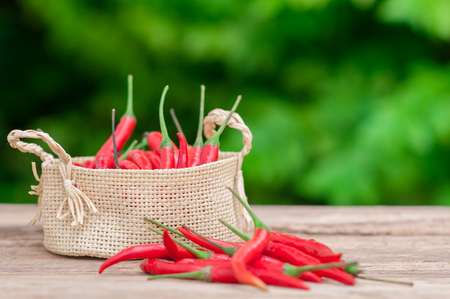 Red hot chili peppers in basket on wooden table with nature background.の写真素材