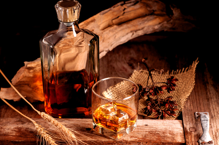 Glass of whiskey with ice decanter on wooden table.の写真素材
