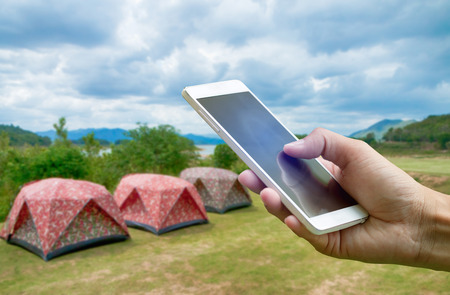 Hand holding smartphone on blurred Tent camping at Keang Kra Jan National park in Petchaburi province Thailandの写真素材
