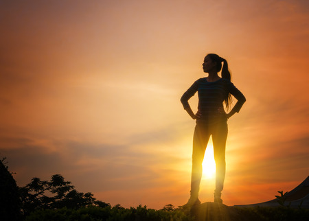 Woman standing on the rock at sunset backgroundの写真素材