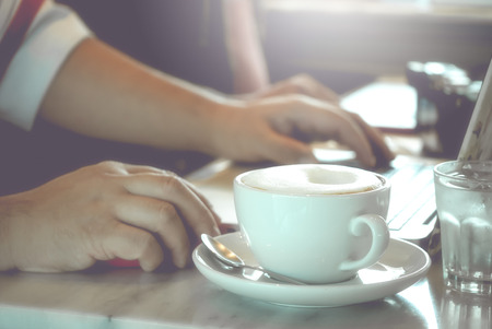 Cup of capuccino on the table with man using laptop in vintage color workplaceの写真素材