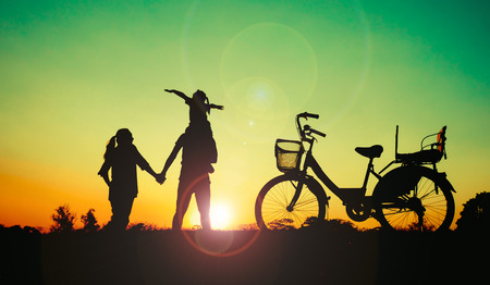 Silhouette happy family father,mother and daughter with bicycle in the park at sunset with sun flareの写真素材