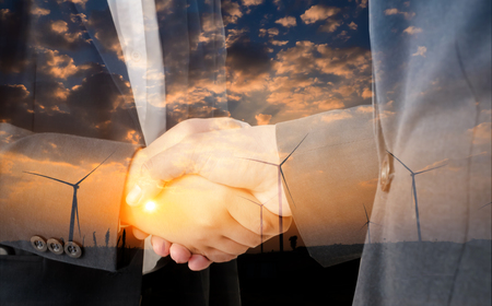 Double exposure of businessman shaking hand with wind turbine natural energy background.の写真素材