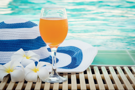 Beach hat,plumeria flower and orange juice near the swimming poolの写真素材
