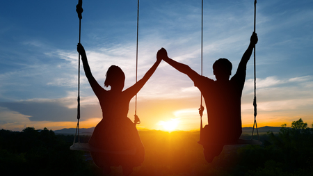 Couples sit on swings and join hands. On the background of the sunset.の写真素材