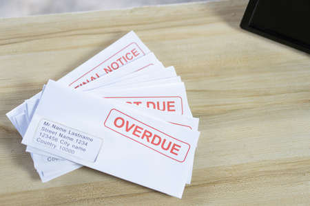 Debt letters that are collected on past overdue bills and final announcements on the table. Red writing to represent the struggle against economic unemployment.の写真素材