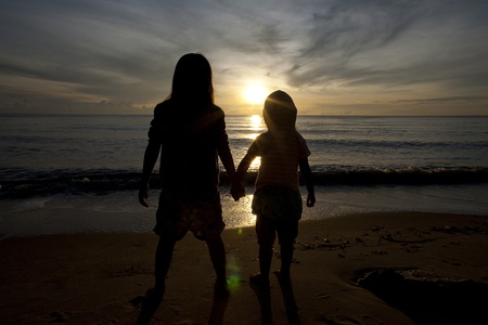 two sisters holding hands and look forward to the sea in Silhouette image.の写真素材