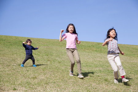 three kids running down from green hillの写真素材