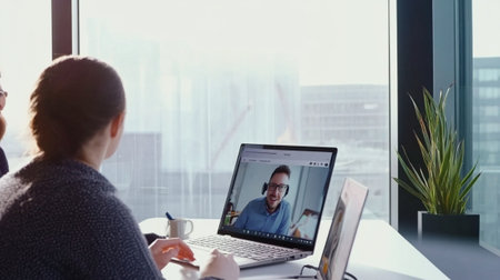 A modern office scene highlighting remote work collaboration through a video conference. Professionals engage in discussion with bright office light and plants in the background.の素材