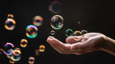 A serene moment captured with floating soap bubbles above an open hand. The colorful bubbles reflect light against a dark background, evoking feelings of joy and wonder.の素材