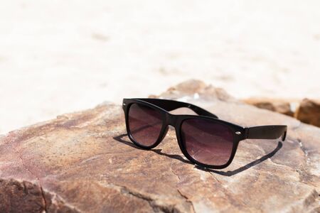 In Summer vacation. The black glasses lying on stone on sea beach.