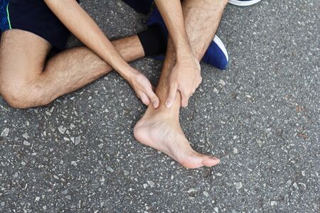 Sport man holding ankle in pain due to sprained ankle. Injury from workout conceptの写真素材