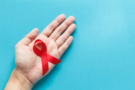 red AIDS awareness ribbon on the hand with blue paper background. World aids day and healthcare and medicine conceptの写真素材