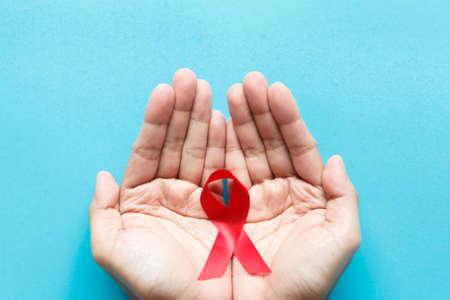 red AIDS awareness ribbon on the hand with blue paper background. World aids day and healthcare and medicine conceptの写真素材