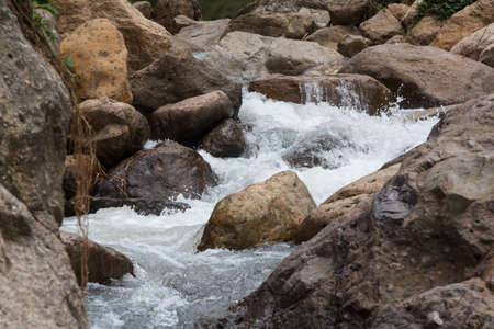 Close up of a little cascade falls of water over mountain river rocks.の写真素材