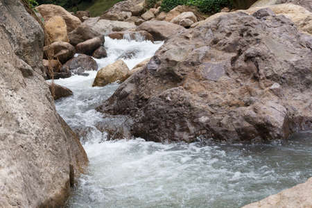 Close up of a little cascade falls of water over mountain river rocks.の写真素材