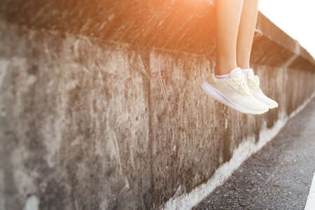 Female is sitting on a wall and hanging the legsの写真素材