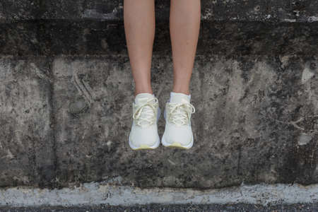 Female is sitting on a wall and hanging the legsの写真素材