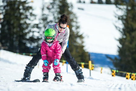 Mother and little child skiing in Alps mountains. Active mom and toddler kid with safety helmet, goggles and poles. Ski lesson for young children. Winter sport for family. Little skier, swiss Alpsの写真素材