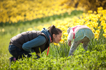 happy cute and beautiful child having fun with mother in yellow flowers in spring in park, cheerful holidays outdoors, healthy lifestyle, loving familyの写真素材