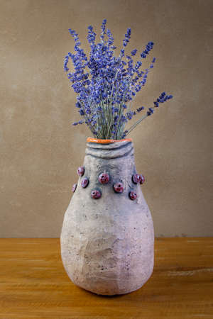 Autumn awesome still life with lavender bouquet  in handmade vase placed on wooden board in front of brown wall with clay plasterの写真素材