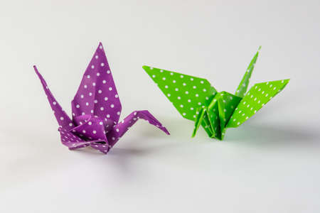 Two origami crain birds made from green and purple paper with white dots, isolated on white backgroundの写真素材