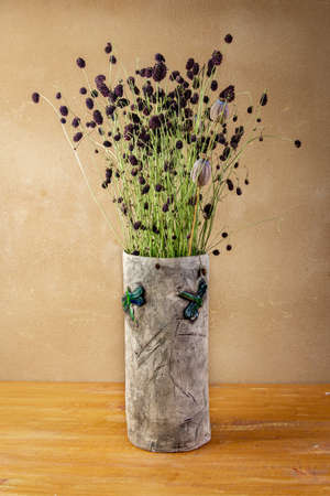 Autumn awesome still life with Sanguisorba officinalis and poppy heads  in handmade ceramic vase with green dragonflies placed on wooden board in front of brown wall with clay plasterの写真素材