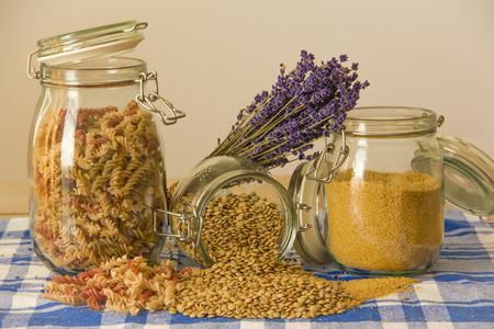 Three jars with pasta, lentils and couscous and lavender on the table. Partly spilled out.の写真素材