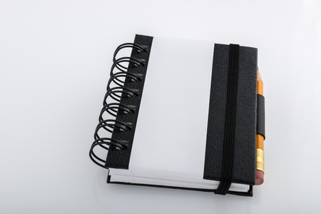 Black and white ringed notepad and pencil resting on a white deskの写真素材