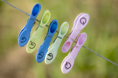 Multi coloured clothing pins attached to a clothing line with a blurred green backgroundの写真素材