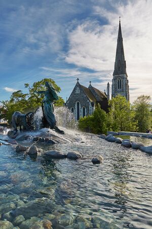 COPENHAGEN, DENMARK - MAY 25, 2017: The Gefion Fountain (Danish: Gefionspringvandet) on the harbor front. It features oxen being driven by the Norse goddess Gefjon. St Alban's Church in the background.のeditorial素材