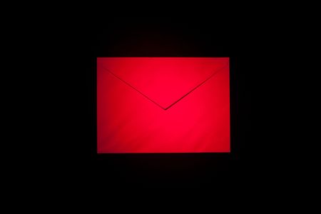closed envelope with red spot light on black backgroundの写真素材